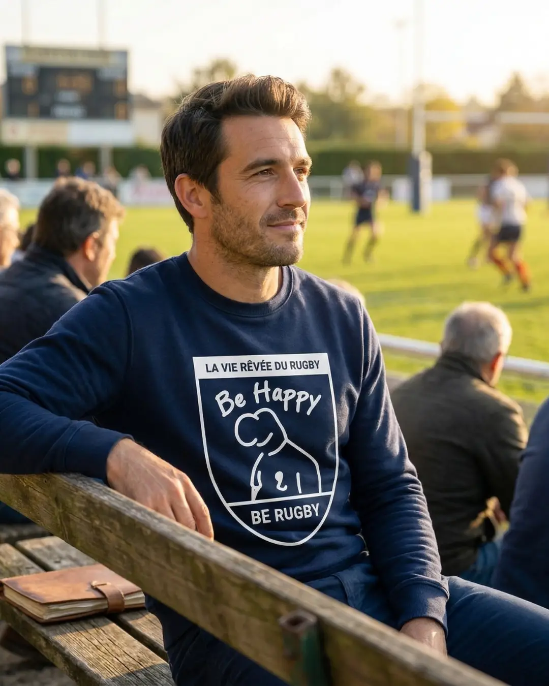 Ancien joueur de rugby amateur assis au bord du terrain portant un sweat Be Happy Be Rugby