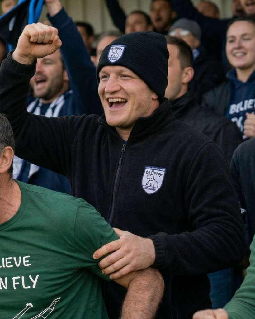 Supporter de rugby amateur en tribune portant une polaire et un bonnet encourageant son équipe pendant un match